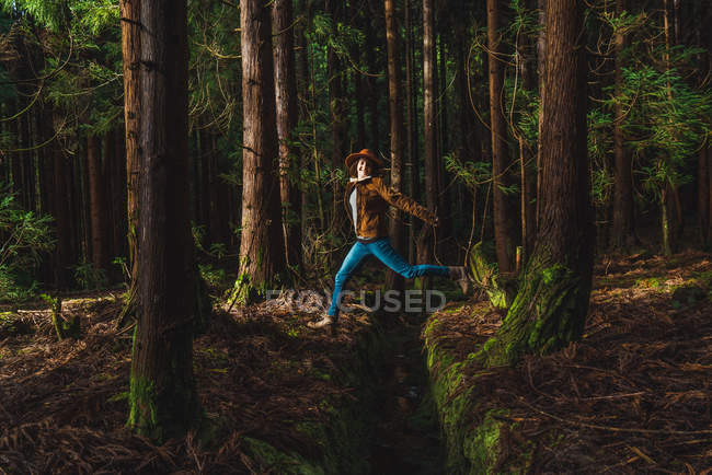 Felice giovane donna saltando oltre drenaggio nella foresta — Foto stock