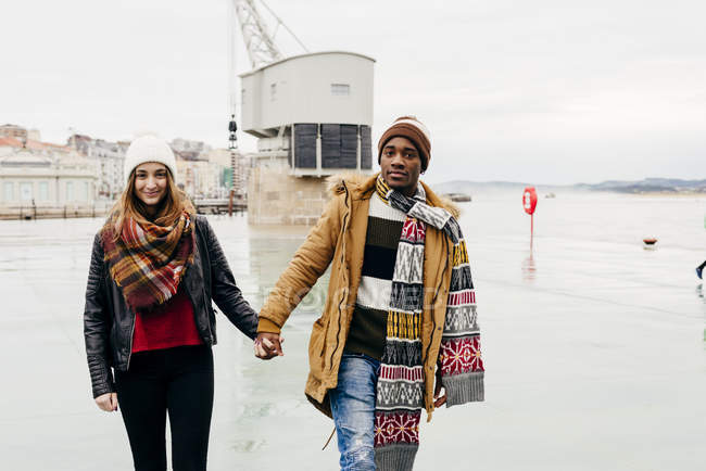 Young multiracial couple standing and holding hands in harbor. — Stock Photo
