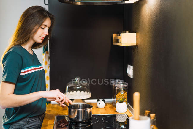Vista lateral da mulher mexendo comida na panela no cozinheiro na cozinha . — Fotografia de Stock