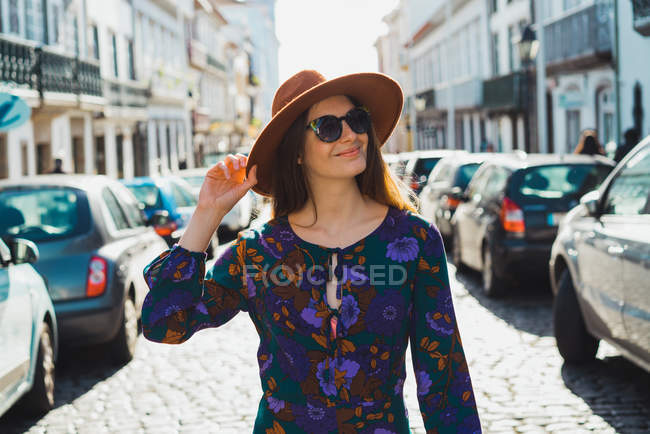 Mulher elegante alegre em chapéu andando em ruas iluminadas pelo sol — Fotografia de Stock