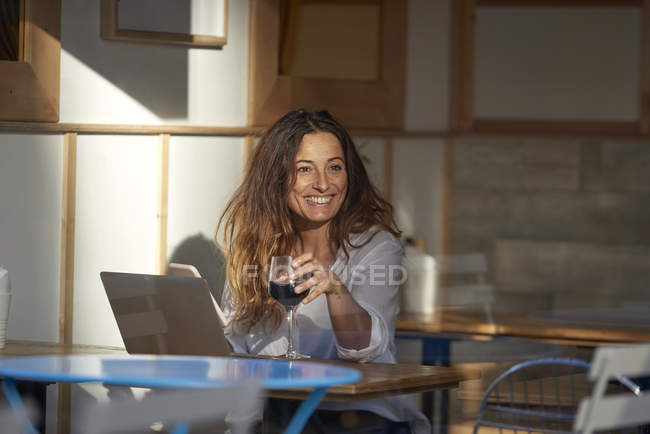 Жінка п'є вино і використовує ноутбук у кафе — стокове фото