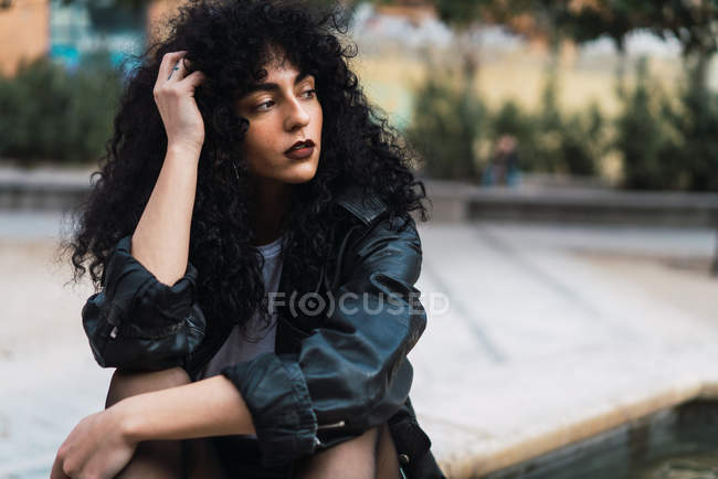 Curly woman sitting on ground on background of city park — Stock Photo