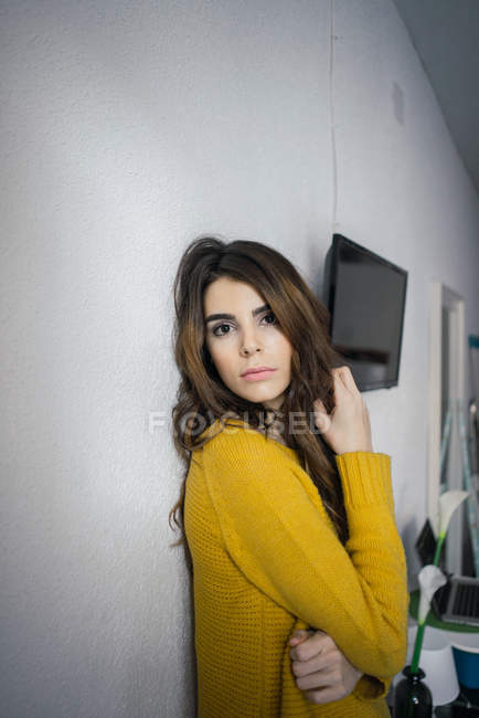 Hübsche Frau im Pullover lehnt an der Wand und blickt in die Kamera — Stockfoto