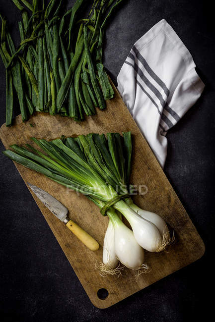 Um monte de cebolas frescas na tábua de corte à mesa escura . — Fotografia de Stock