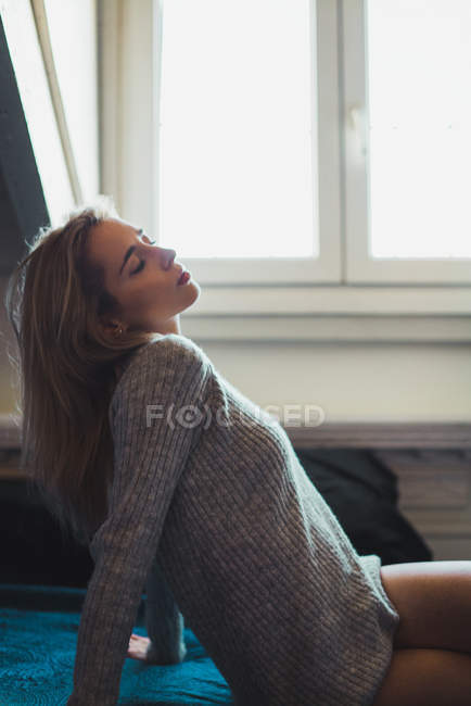 Молодая блондинка сидит на кровати с закрытыми глазами — стоковое фото