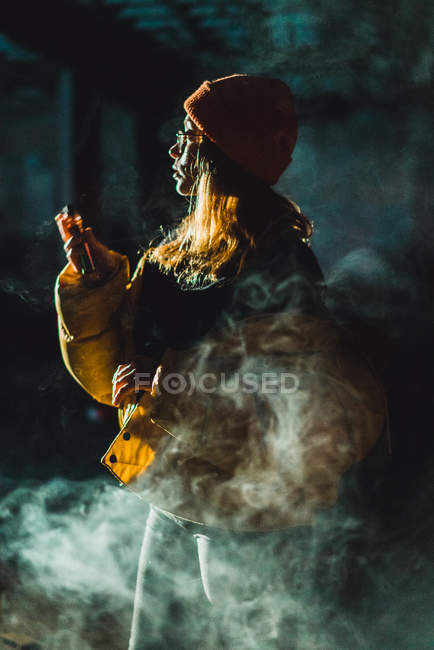 Woman posing in yellow jacket and vaping in abandoned building — Stock Photo