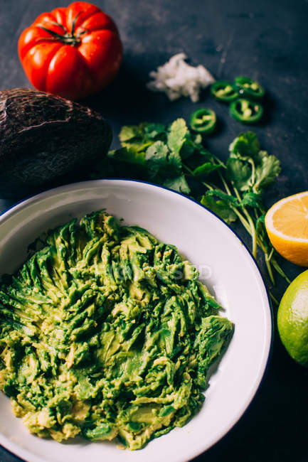 Ceramic plate with guacamole on table with ingredients — Stock Photo