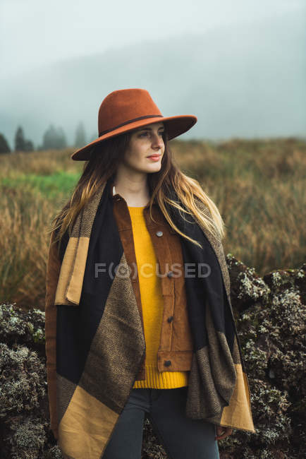Jeune brune en écharpe tendance et chapeau debout sur le terrain — Photo de stock