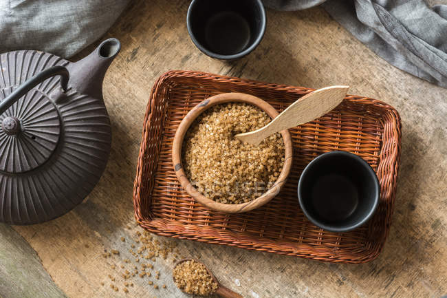 Directly above view of bowl full of brown sugar on wicker tray and tea cups — Stock Photo
