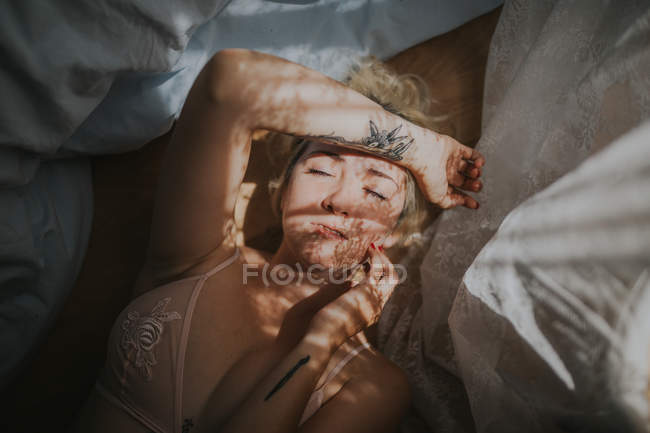 Portrait of blonde woman in bed with curtain shadow on face — Stock Photo