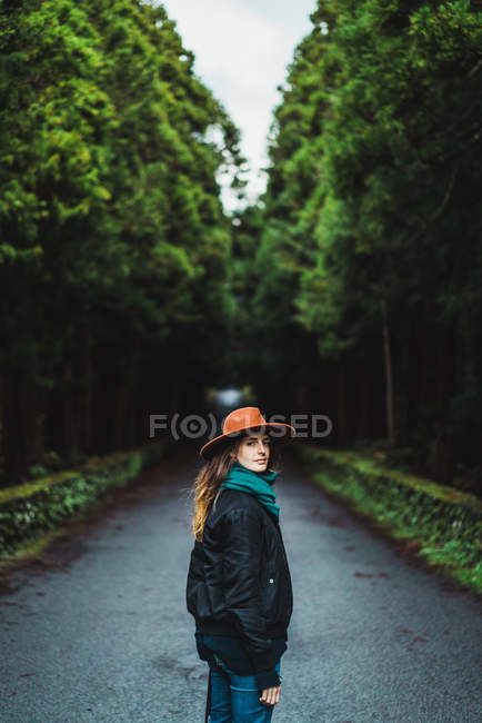 Vista laterale della donna in cappello in posa sulla strada forestale — Foto stock