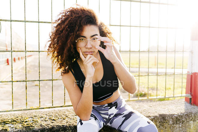 Jeune femme assise à la grille et tenant le menton sur la main — Photo de stock
