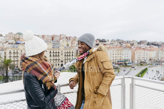 Cheerful girl pulling scarf of boyfriend on background of city. — Stock Photo