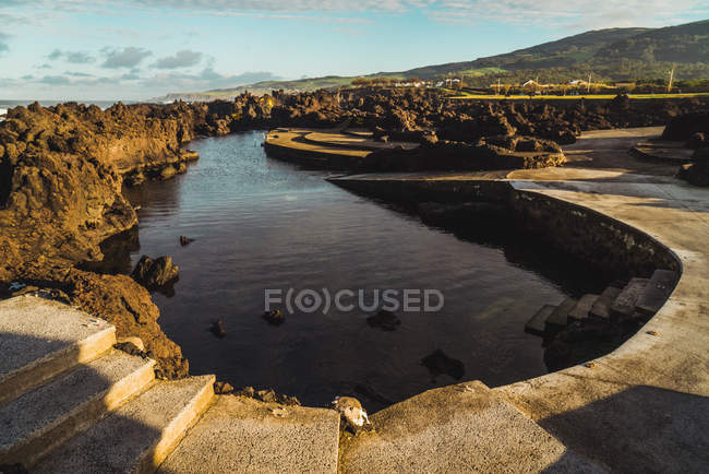 Escalones de hormigón y pequeño estanque redondeado con rocas en la naturaleza . - foto de stock