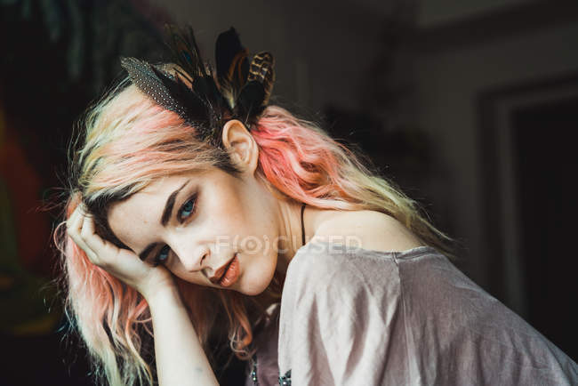 Mujer atractiva con el pelo rosa y plumas mirando a la cámara - foto de stock