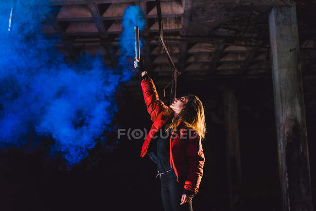 Femme posant avec une torche bleue fumant dans un bâtiment abandonné — Photo de stock