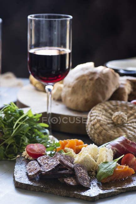 Tasty snacks on stone plate and glass of red wine — Stock Photo