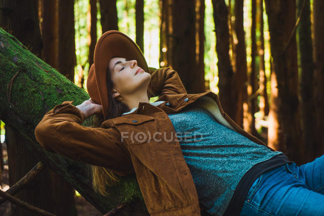 Молода жінка розслабляється з закритими очима на стовбурі дерева в лісі . — стокове фото