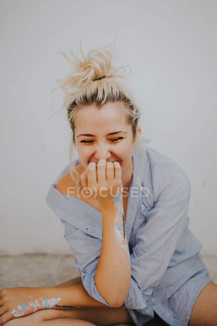 Mujer riendo en camisa masculina sentada en la pared blanca - foto de stock