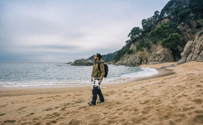 Homem com mochila andando na praia com drone na mão — Fotografia de Stock