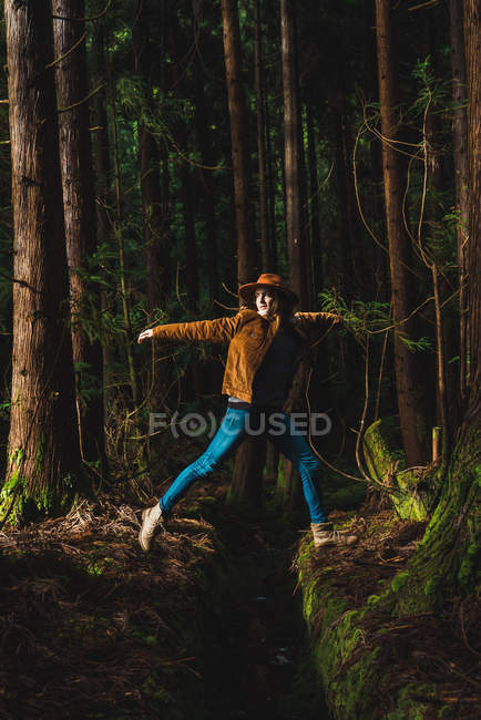 Vista lateral da jovem mulher pulando sobre o dreno na floresta verde . — Fotografia de Stock