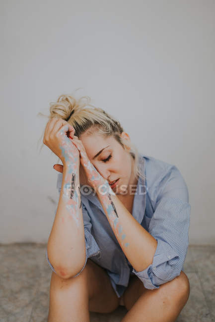 Müde blonde Frau im Männerhemd sitzt an der Wand — Stockfoto