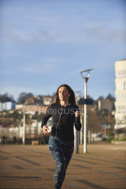 Femme dans les écouteurs fonctionnant sur la scène urbaine — Photo de stock