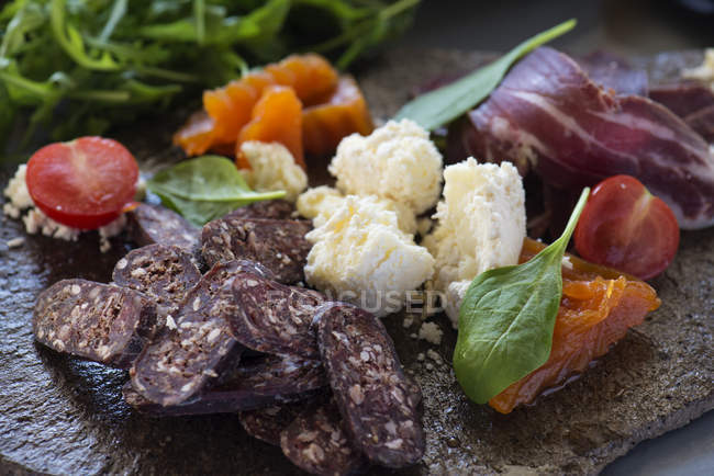 Vista ravvicinata dei prodotti di prelibatezza della carne con formaggi e verdure su piatto di pietra . — Foto stock