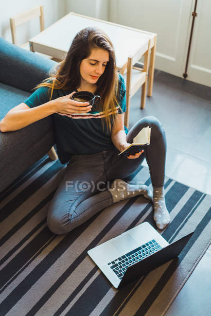 Молода жінка, сидячи на підлозі, ноутбук з блокнота в руках вдома — стокове фото