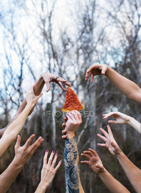 Colpo di raccolto di persona tatuata che tiene fetta di pizza e le mani cercando di raggiungerlo in lotta. — Foto stock