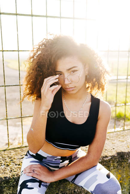 Mujer joven sentada en la rejilla y posando ante la cámara - foto de stock