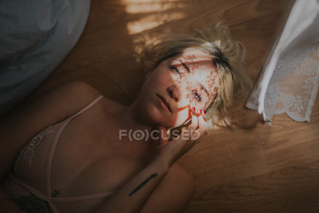Чувственная женщина лежит на кровати с тенью от занавеса на лице — стоковое фото