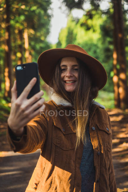 Jovem alegre tomando selfie na floresta iluminada pelo sol . — Fotografia de Stock
