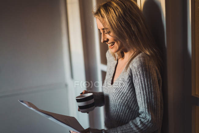 Smiling woman with cup reading papers — Stock Photo