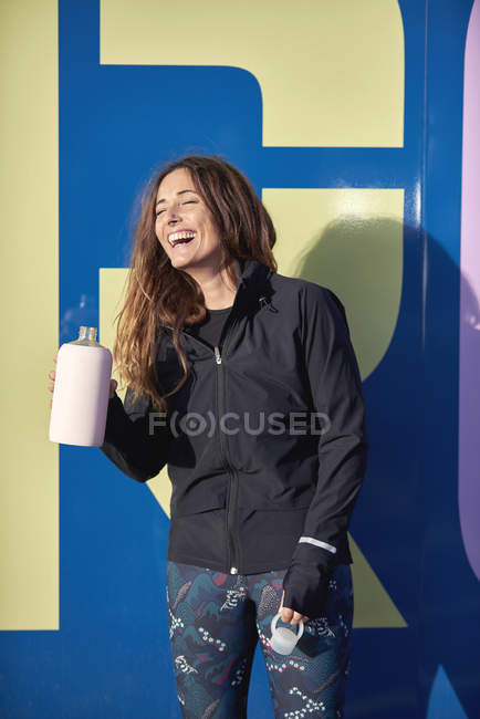 Спортивна жінка сміється і п'є зі спортивної пляшки — стокове фото