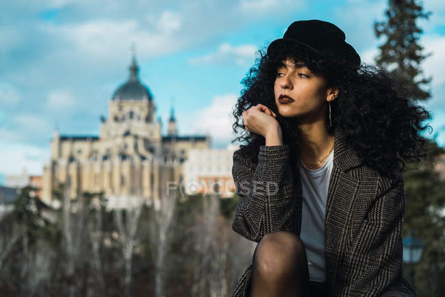 Молода кучерява жінка сидить на фоні витіючого фасаду в сутінках — стокове фото