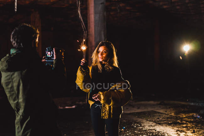 Задний вид фотографа, делающего снимки довольно стильной женщины с зажиганием искры в заброшенном здании
. — стоковое фото
