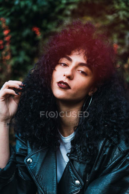 Portrait of young curly woman posing in park and looking at camera — Stock Photo