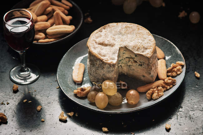 Натюрморт тарелки с голубым сыром и виноградом, грецкие орехи на темном столе — стоковое фото