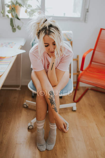 Hübsche blonde Frau mit tätowiertem Arm sitzt zu Hause auf Stuhl. — Stockfoto