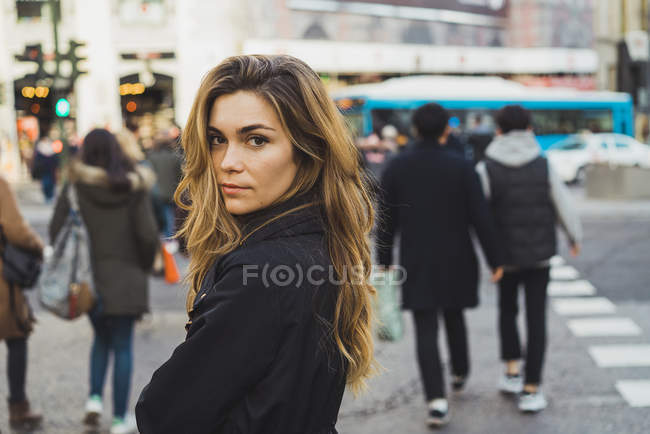 Женщина смотрит через плечо на камеру на улице — стоковое фото