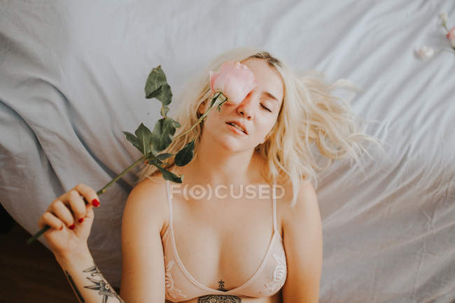 Sinnliche Frau im Bett liegend mit Rose im Gesicht — Stockfoto
