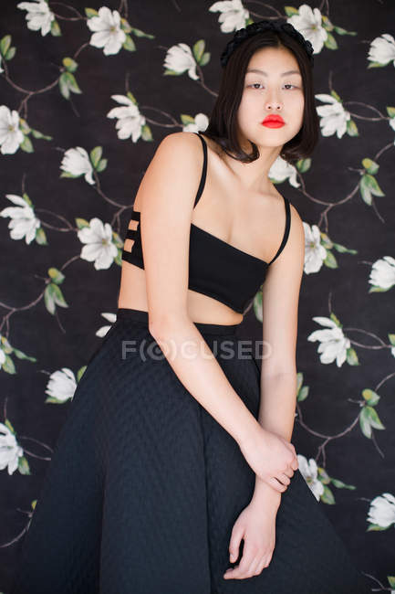 Mujer bonita con labios rojos con ropa negra posando sobre fondo floral - foto de stock