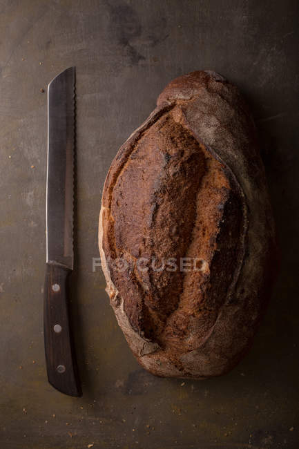 Свежеиспеченный хлеб и нож на коричневом столе — стоковое фото