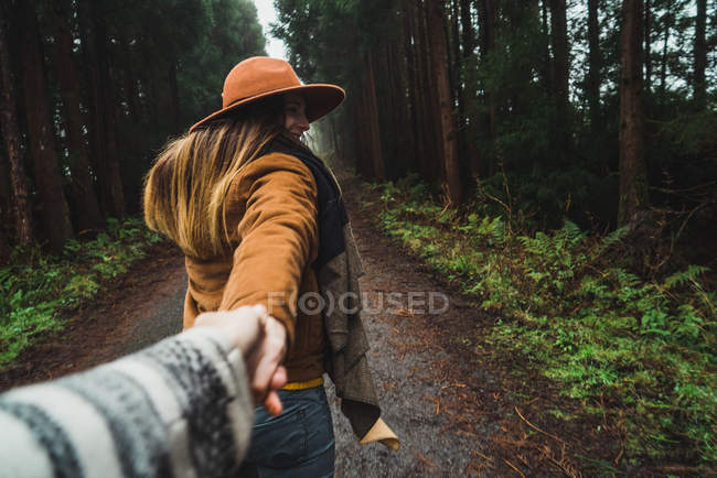 Back view of stylish woman in jacket asking to follow her into beautiful green woods. — Stock Photo