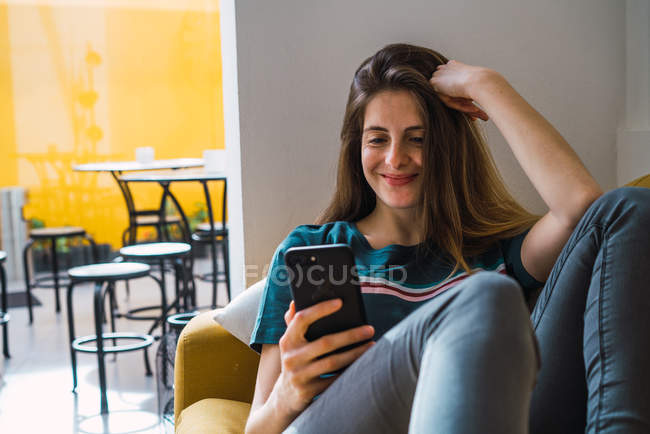 Молодая улыбающаяся женщина лежит на диване и просматривает смартфон — стоковое фото