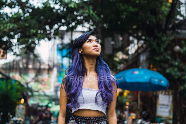 Мрійлива жінка з фіолетовим волоссям, що стоїть на вулиці і дивиться в сторону . — стокове фото