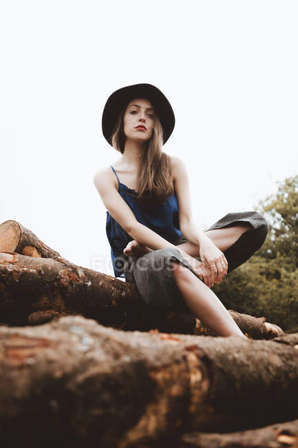 Sensuale donna in cappello seduta sul mucchio di tronchi — Foto stock