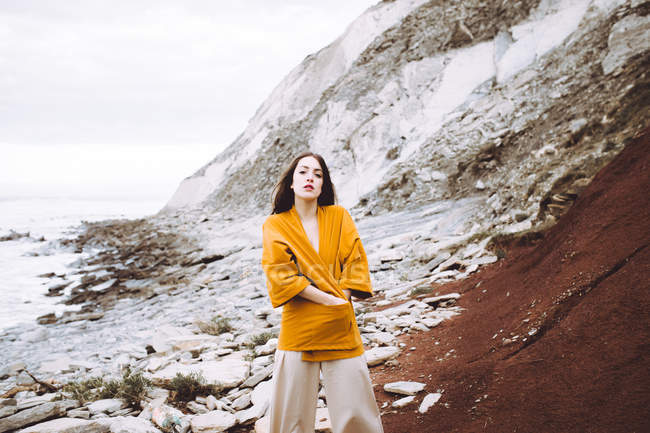 Giovane ragazza bruna in giacca gialla in posa sulla riva — Foto stock