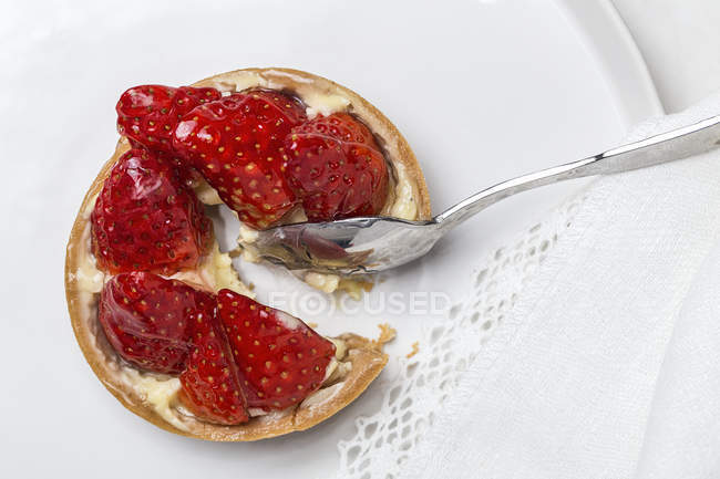 Tart with red strawberry and spoon served on white plate. — Stock Photo